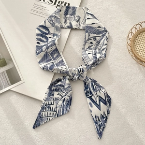 Detailed view of navy blue printed twilly silk scarf tied in a bow on magazine background