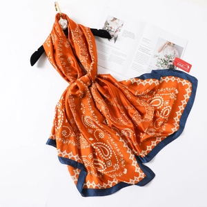 Bohemian orange paisley satin scarf with navy border draped on a wooden hanger