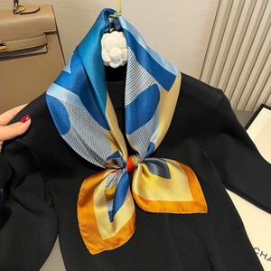 Blue and yellow geometric horse print satin silk scarf styled on a black sweater neckline