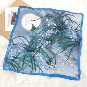 Close-up of elegant floral silk scarf with blue trim and nature landscape print details