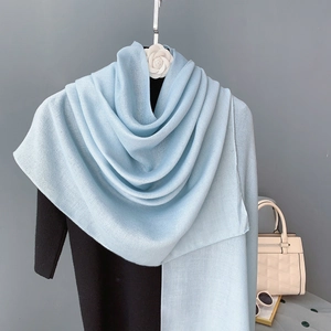 Écharpe et châle en coton bleu clair portés sur un haut noir avec un fond neutre