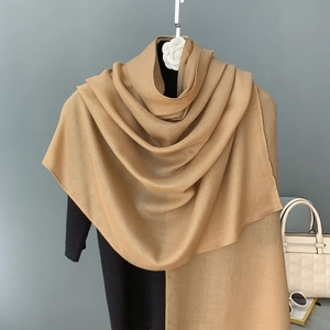 Détail d'une écharpe en coton et lin camel avec une texture tissée sur un manteau noir
