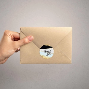 Close-up of circular thank you seal stickers with gold patterns on kraft envelopes