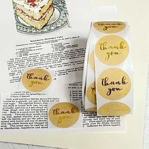 Close-up of round gold foil Thank You stickers on kraft paper for gift packaging