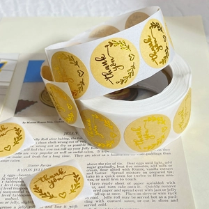 Close-up of gold foil Thank You stickers on a vintage book with floral wreath design