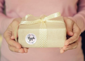Detail of floral Thank You sticker on craft gift box held by hands in warm lighting
