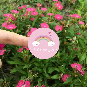 Round pink 'Thank you' sticker with cartoon rainbow and smiling clouds for gift sealing