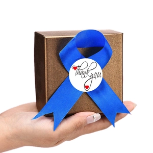 White round Thank You stickers with red hearts on a brown gift box with blue ribbon
