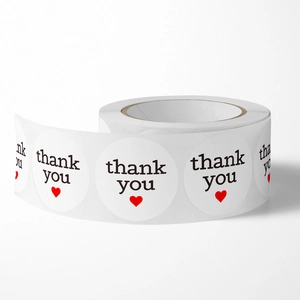 Roll of white circular thank you stickers with black text and a small red heart icon