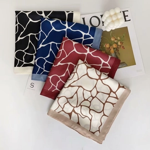 Detailed view of square silk scarves with abstract patterns and brand tags on a magazine