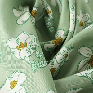 Detailed close-up of light green floral silk scarf with twill texture and soft drape