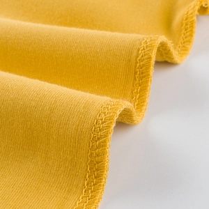 Detailaufnahme eines senfgelben Baumwoll-Strickshirts mit hochwertiger Overlock-Nahtführung