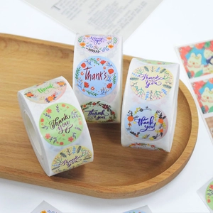Detailed close-up of three rolls of floral Thank You stickers on a wooden tray