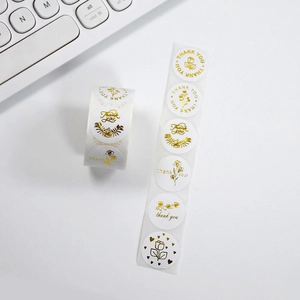 Detail of round white and gold foil Thank You stickers with floral patterns on a roll