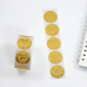 Macro shot of gold foil 'Thank You' stickers with floral wreath on kraft paper background