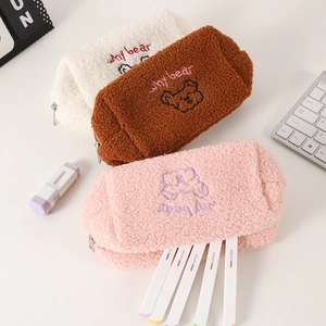 Three plush teddy fleece pencil cases with bear embroidery on a clean desk workspace