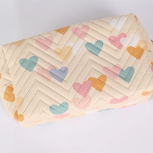Detailed close-up of cream ruffled pencil case with colorful macaron heart embroidery