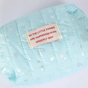 Close-up of light blue quilted pencil case with shiny silver heart patterns and woven label