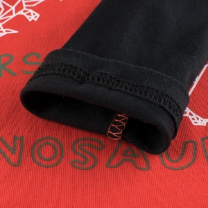 Close-up of boys red cotton long sleeve T-shirt with dinosaur print and black cuffs