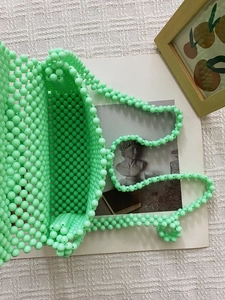 Top view of a mint green beaded woven bag on white fabric with artistic paper props