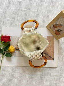 Detail of hand-woven faux pearl handbag with amber-textured acrylic round handles