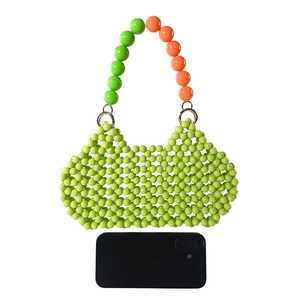 Close-up of a handmade green acrylic beaded handbag with orange handles and phone for scale