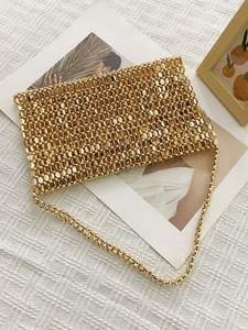 Detail of hand-woven gold metal sequin tote bag with sleek chain strap on white fabric