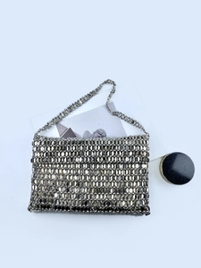 Detailed view of silver metal sequin woven handbag with slender chain strap on white background