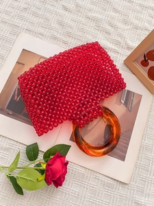 Sac à main artisanal en perles rouges avec anses rondes ambrées sur fond rustique chic
