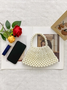 Detail einer handgefertigten Mini-Perlen-Handtasche mit rundem Griff auf weißem Stoff