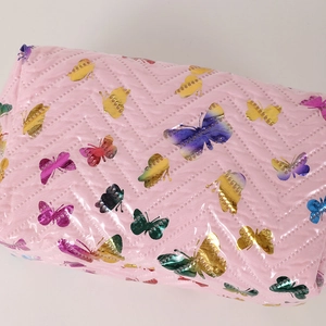 Macro shot of pink quilted fabric with colorful metallic butterfly details and stitching