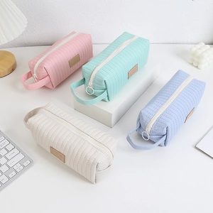 Close-up of pastel quilted pencil cases with zipper pulls and side handles on a desk