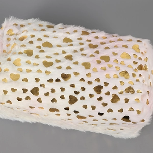 Macro detail of white faux fur pouch featuring shiny gold heart-shaped metallic patterns