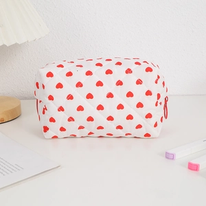 Detailed view of white quilted cosmetic bag with red heart pattern and zip closure