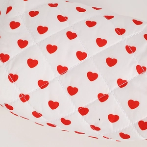 Close-up of white quilted fabric with red heart patterns and neat diamond stitching detail