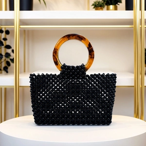 Détail du sac perlé avec des perles noires brillantes et des anses en acrylique écaille
