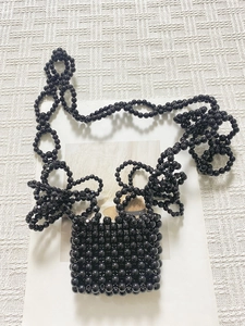 Dettaglio della mini borsa di perline nere intrecciate con decori floreali sulla tracolla
