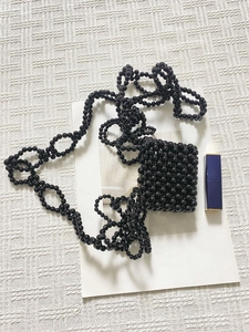 Dettaglio di mini borsa in perline nere intrecciate a mano con finitura lucida e tracolla