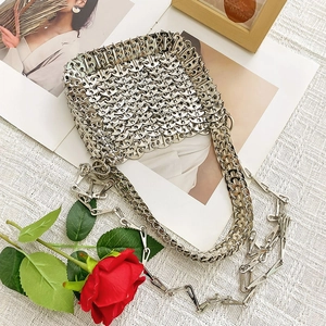 Detail of silver sequin woven bag with metal chain strap and red rose on white fabric