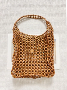 Detailed view of bohemian hand-woven wooden bead handbag on a textured white fabric background