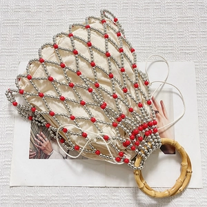 Detail of woven faux pearl bucket bag with red accents and natural bamboo handles