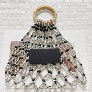 Detail of silver and black beaded mesh bag featuring a natural bamboo top handle