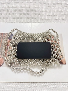 Silver metal beaded hollow-out shoulder bag with mesh structure shown with a smartphone