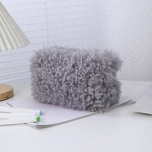 Detailed view of gray plush makeup bag with zipper closure on a white desk with shadows