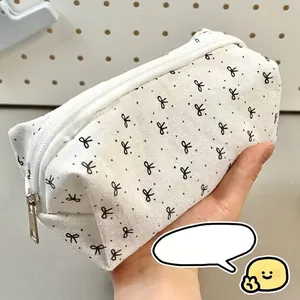 Minimalist cream canvas pencil case with black bow patterns held in hand by a student