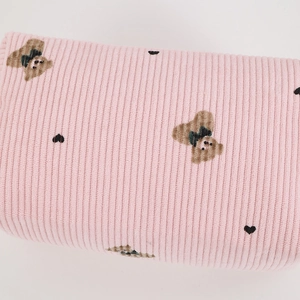 Detailed close-up of pink corduroy fabric with cute bear and heart patterns on makeup bag