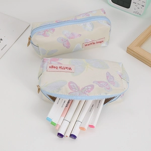 Detail of butterfly embossed pencil case with gold zipper and waffle label on white desk