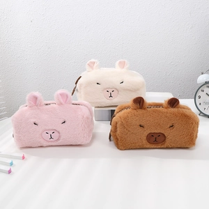 Three plush Capybara pencil cases in pink, beige, and brown on a white desktop