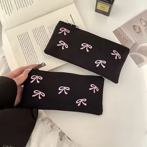 Detail view of black fabric pencil case featuring pink bow embroidery and metal zipper