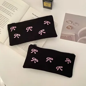 Set of two black canvas pencil cases featuring pink bow embroidery and zipper closure